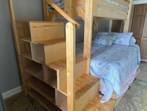 Ein Etagenbett mit Holzleiter und Ablagefläche, eine geblümte Bettdecke und ein Teppichboden.