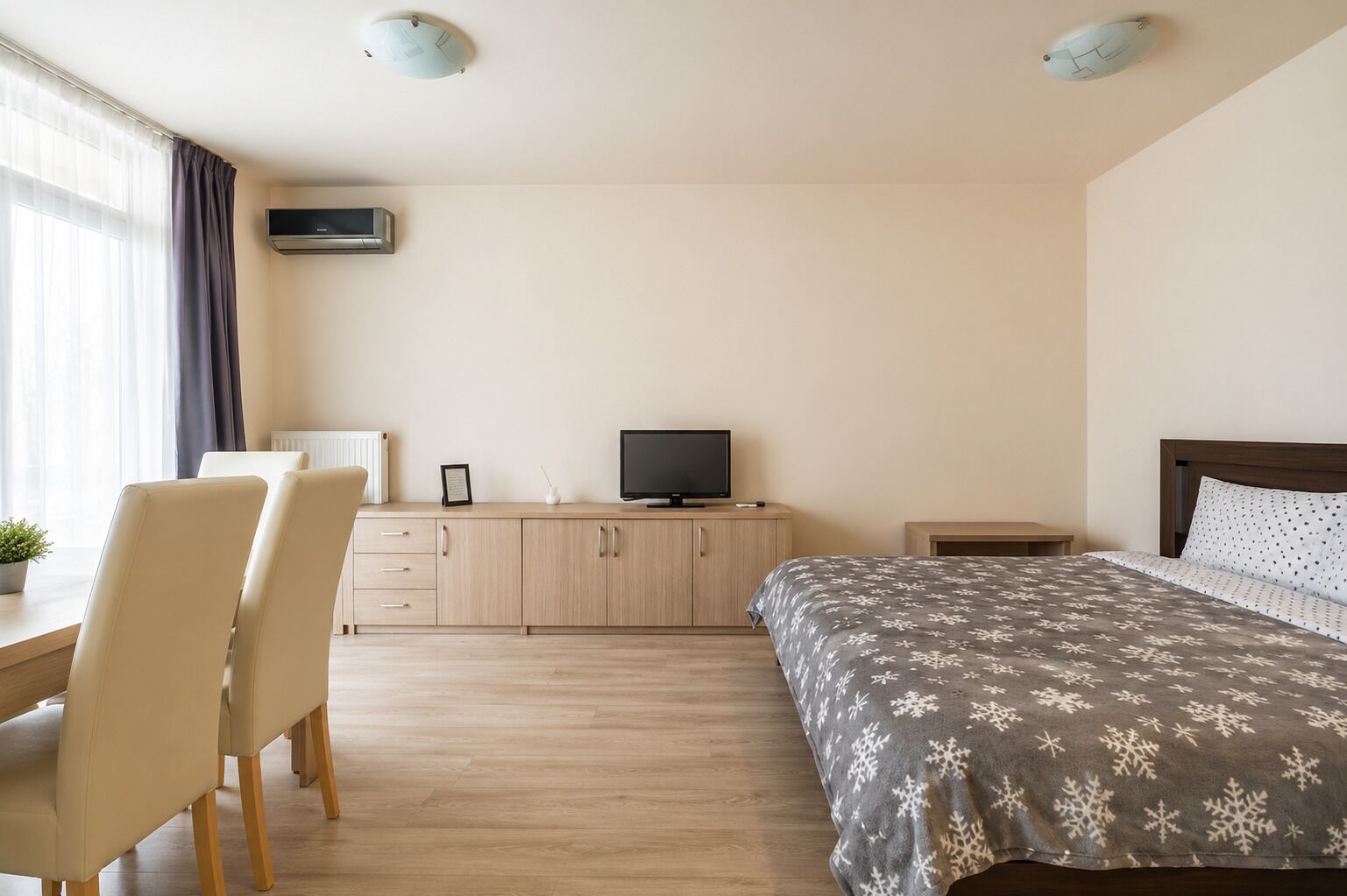 A hotel room with a bed, a desk with chairs, a television, and a bedside table.