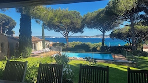 Ett poolområde med utsikt över havet, omgivet av träd och ett hus.
