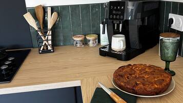 Una cocina con cafetera, utensilios de madera, frascos, un pastel y un vaso de vidrio verde.