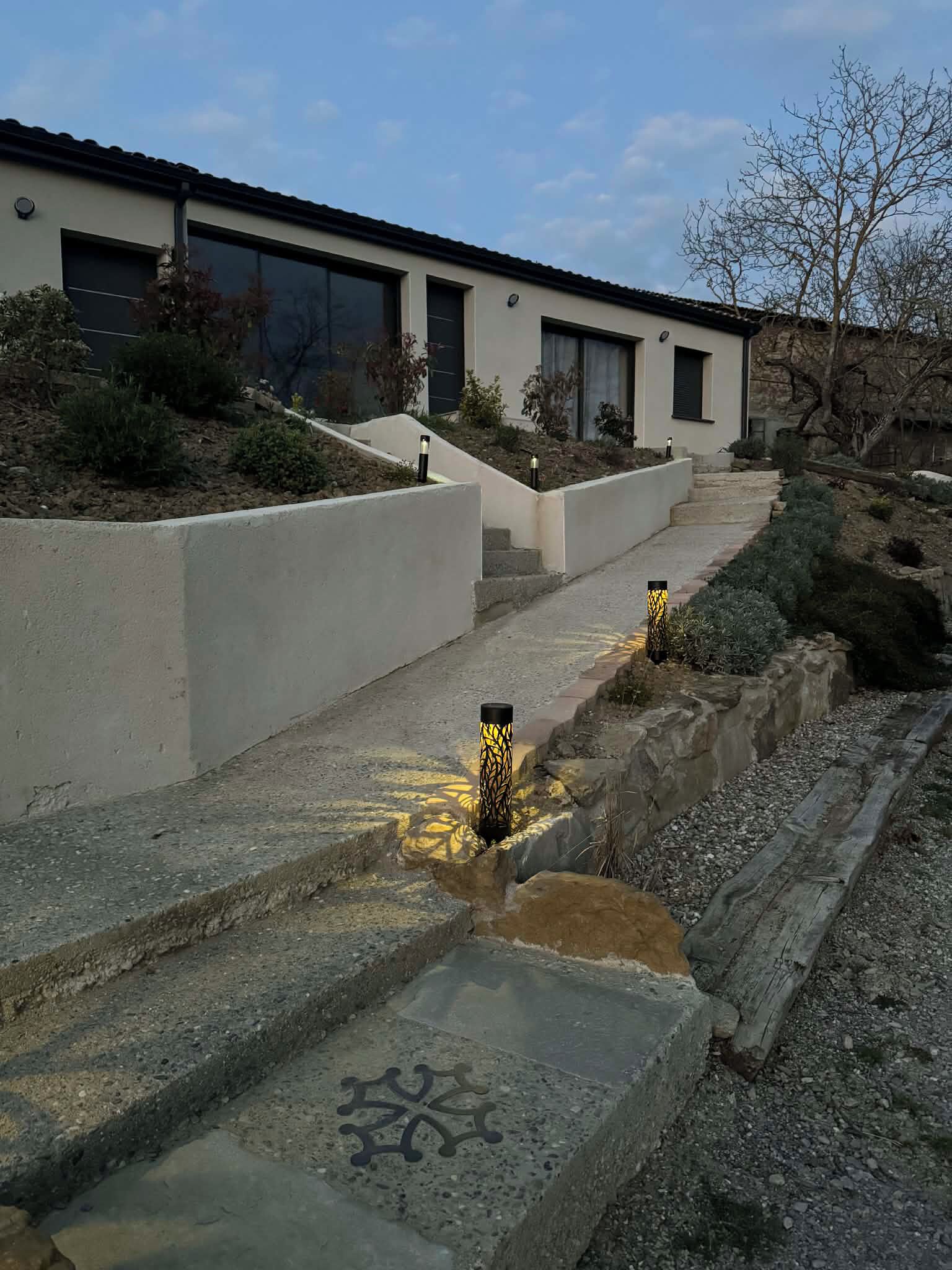 A modern building with a concrete pathway leading to the entrance, surrounded by landscaped areas and a stone retaining wall.