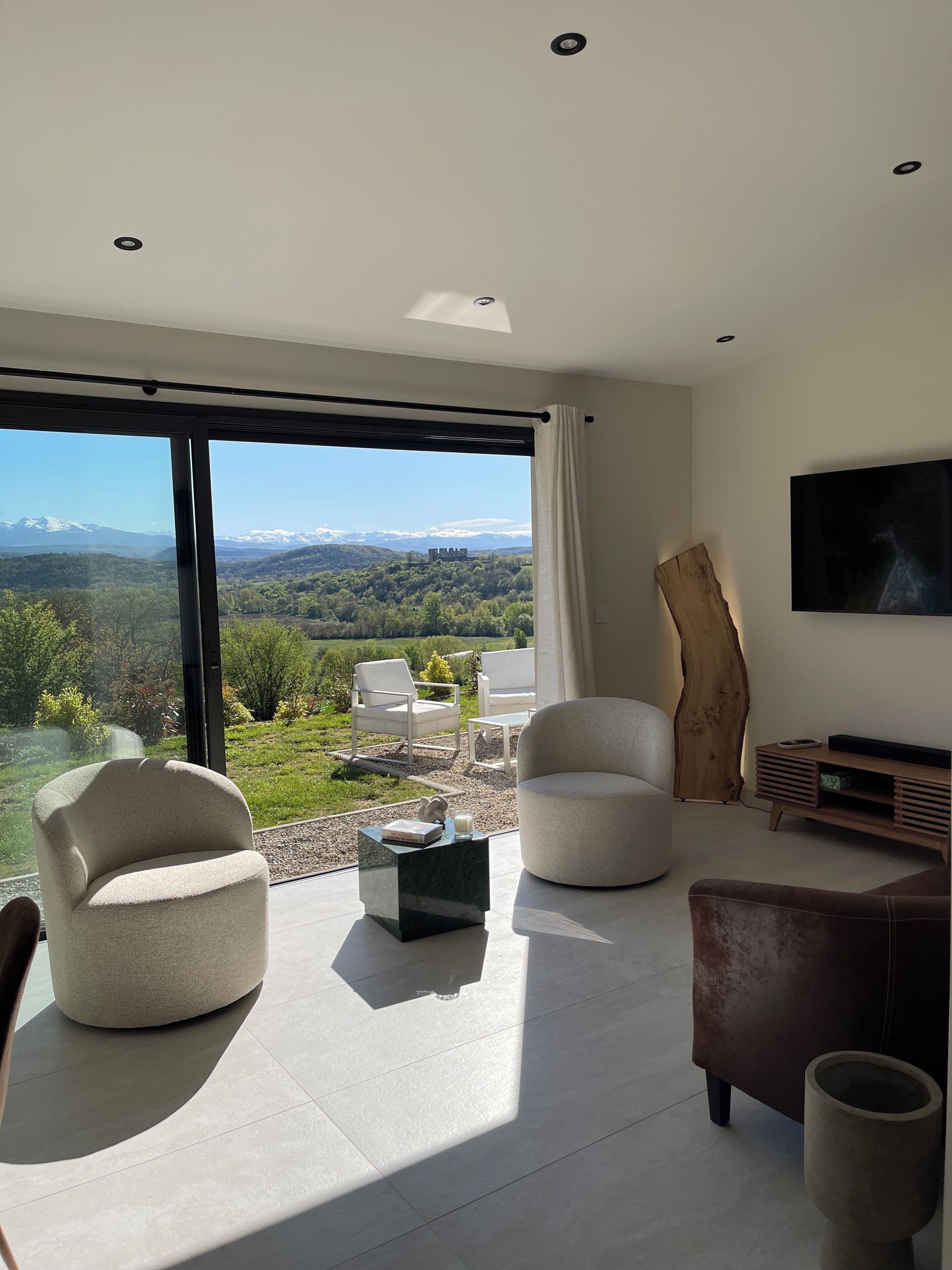 A modern living room with a large window, a flat-screen TV, and a wooden accent piece.