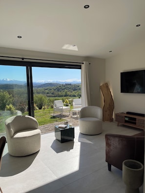 Una sala de estar moderna con un ventanal grande, un televisor de pantalla plana y un detalle decorativo de madera.
