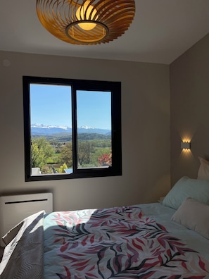 A bedroom with a bed, a window with a view of mountains, a wall-mounted light, and a ceiling light fixture. - A getaway with a view of the Pyrenees: Spa & Sauna. Exceptional Vacation Rental (Tréziers)