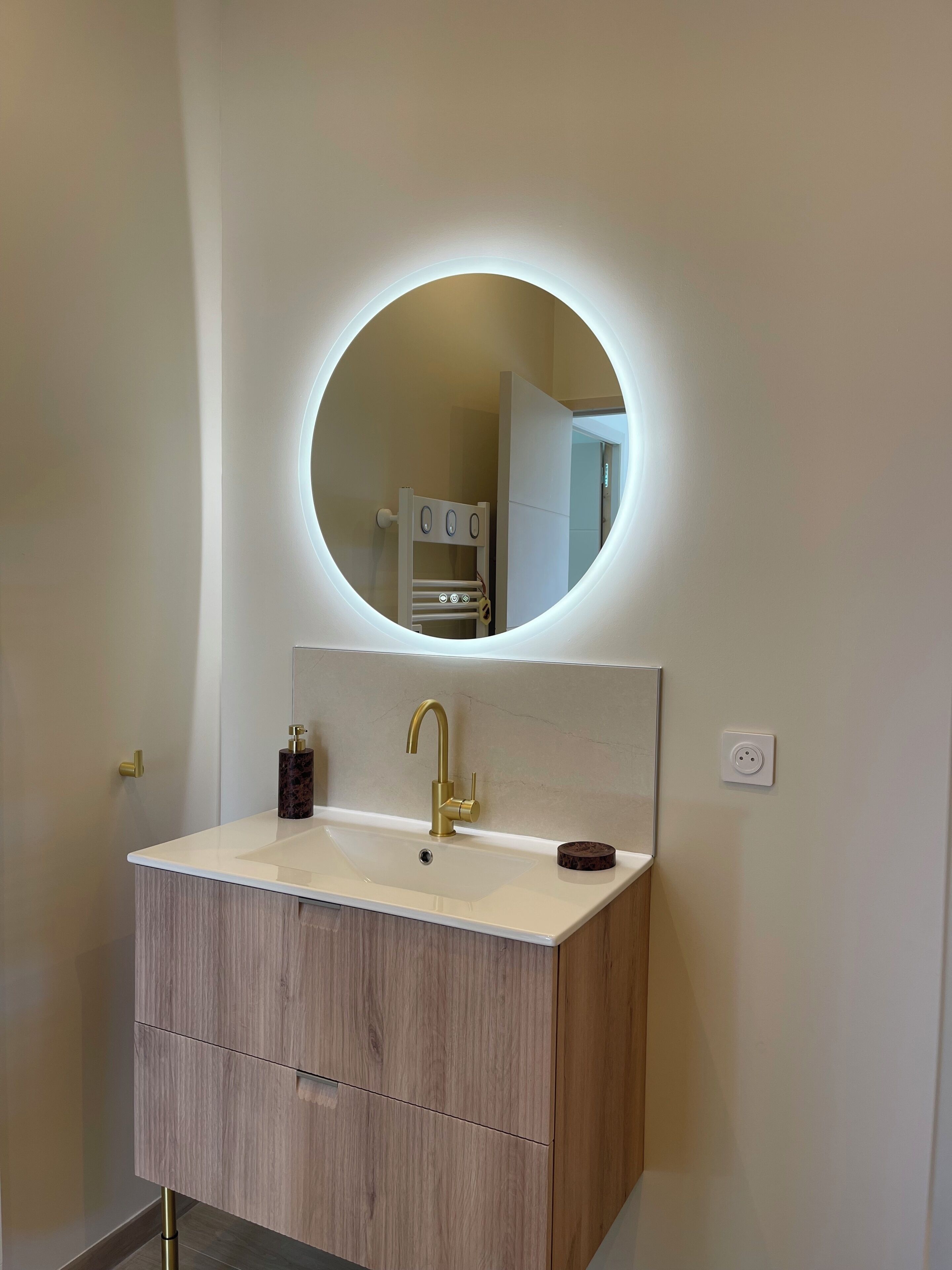 Un baño con un espejo redondo, un grifo dorado y un tocador de madera.