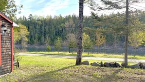 A rustic cabin with a wooden exterior, a paved path, and a natural landscape with trees and a body of water in the background.