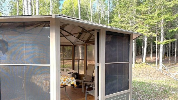 A screened porch with a table and chairs, surrounded by trees.