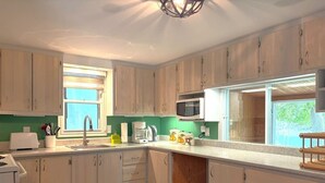 A kitchen with wooden cabinets, a microwave, a sink, and a window.