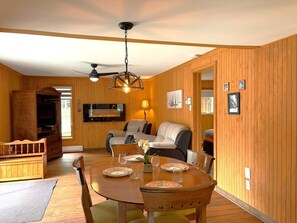 A wooden-paneled room with a dining table set for four, a sofa, and a television.
