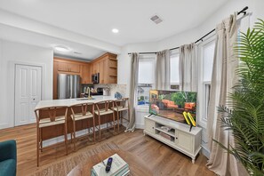 Una cocina moderna con armarios de madera, un refrigerador de acero inoxidable y una zona de comedor con una mesa y sillas blancas.