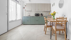 A modern kitchen with light-colored cabinets, a dining table with chairs, and a window with curtains.
