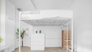 A bunk bed with a white headboard, a white dresser, and a wooden shelf unit in a minimalist room.