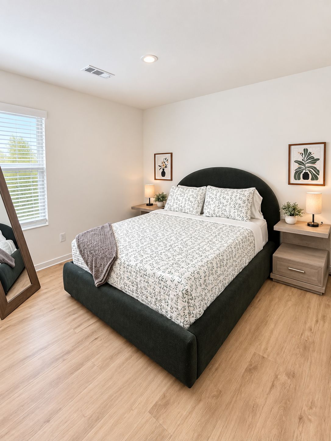 A modern bedroom with a bed, bedside tables, a mirror, and artwork on the walls.