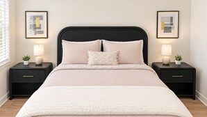A bed with a black headboard, two bedside tables with lamps, and framed artwork on the walls.