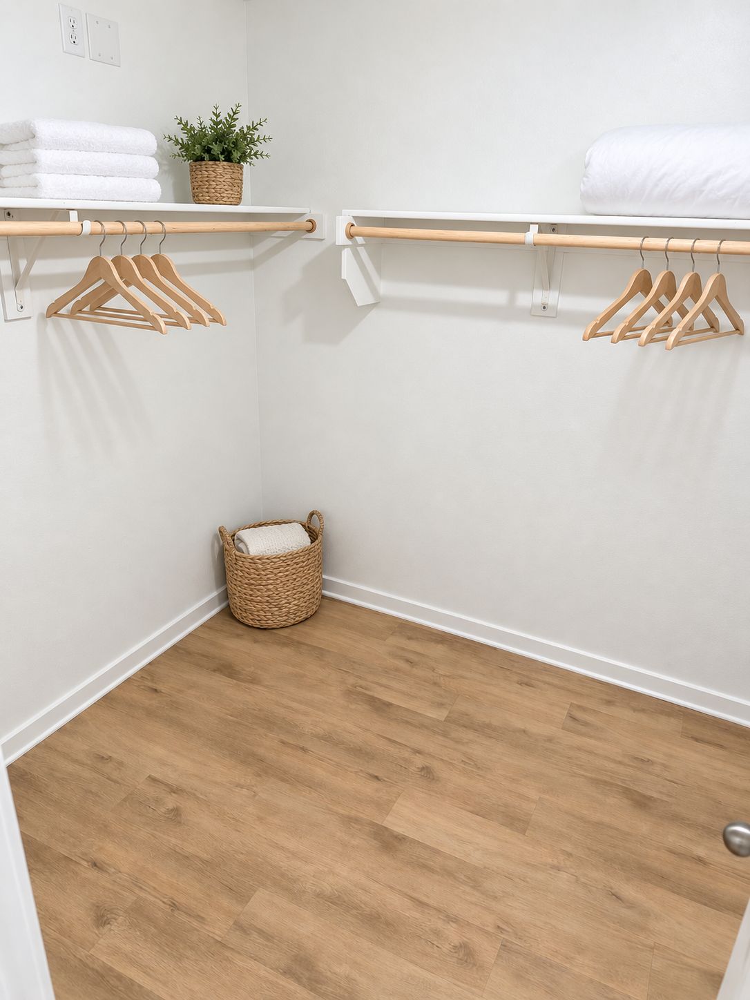 Een kleine, netjes geordende kast met houten hangers, een witte handdoek en een gevlochten mand.
