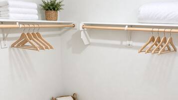 Een kleine, netjes geordende kast met houten hangers, een witte handdoek en een gevlochten mand.