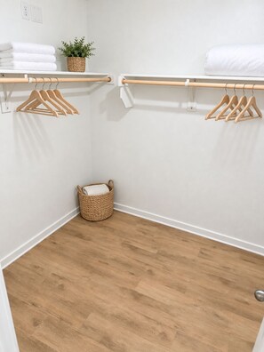 Armário pequeno e bem organizado com cabides de madeira, uma toalha branca e uma cesta de fibra natural.
