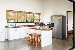 A modern kitchen with white cabinets, a wooden countertop, a stainless steel refrigerator, and a window with bamboo blinds. - Private Villa near Santa Teresa with Ocean View, Pool & King Suites (Provincia de Puntarenas)