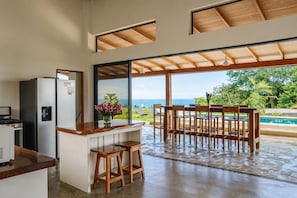 Eine Küche mit Blick auf Pool und Grünflächen, ein Essbereich mit Holzmöbeln und ein großes Fenster.