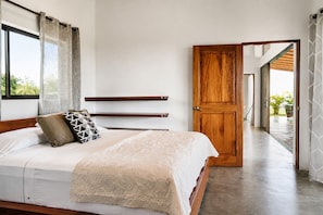 Ein Schlafzimmer mit einem großen Bett, einer Holztür und Blick ins Freie.