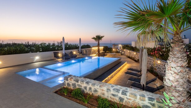 Ein Pool auf dem Dach mit Steinmauern, Liegestühlen und Blick auf das Meer im Dämmerlicht.