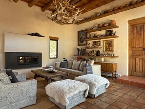 A cozy living room with a fireplace, a sofa, a coffee table, and a decorative antler chandelier.