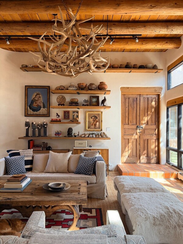 A cozy living room with a wooden ceiling, a large antler chandelier, a sofa set, a coffee table, and a fireplace.
