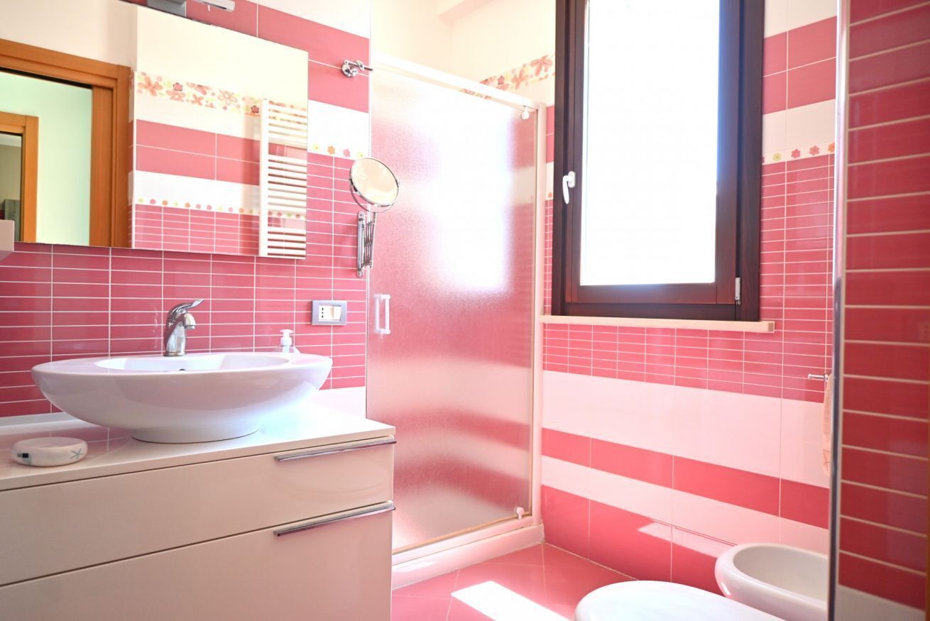 Un bagno con un lavandino bianco, uno specchio, una doccia e un water.