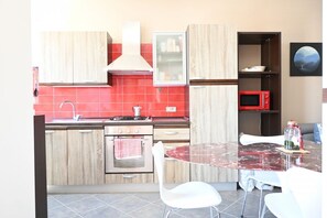 Una cocina moderna con armarios de madera, un salpicadero de azulejos rojos, una estufa a gas, un microondas y un comedor con mesa de vidrio y sillas blancas.