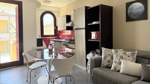 A modern kitchen with a dining area, a sofa with patterned cushions, and a view through an arched window.