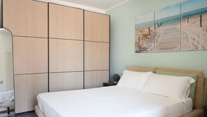 A bedroom with a bed, a wardrobe, a nightstand, and a beach-themed wall art.