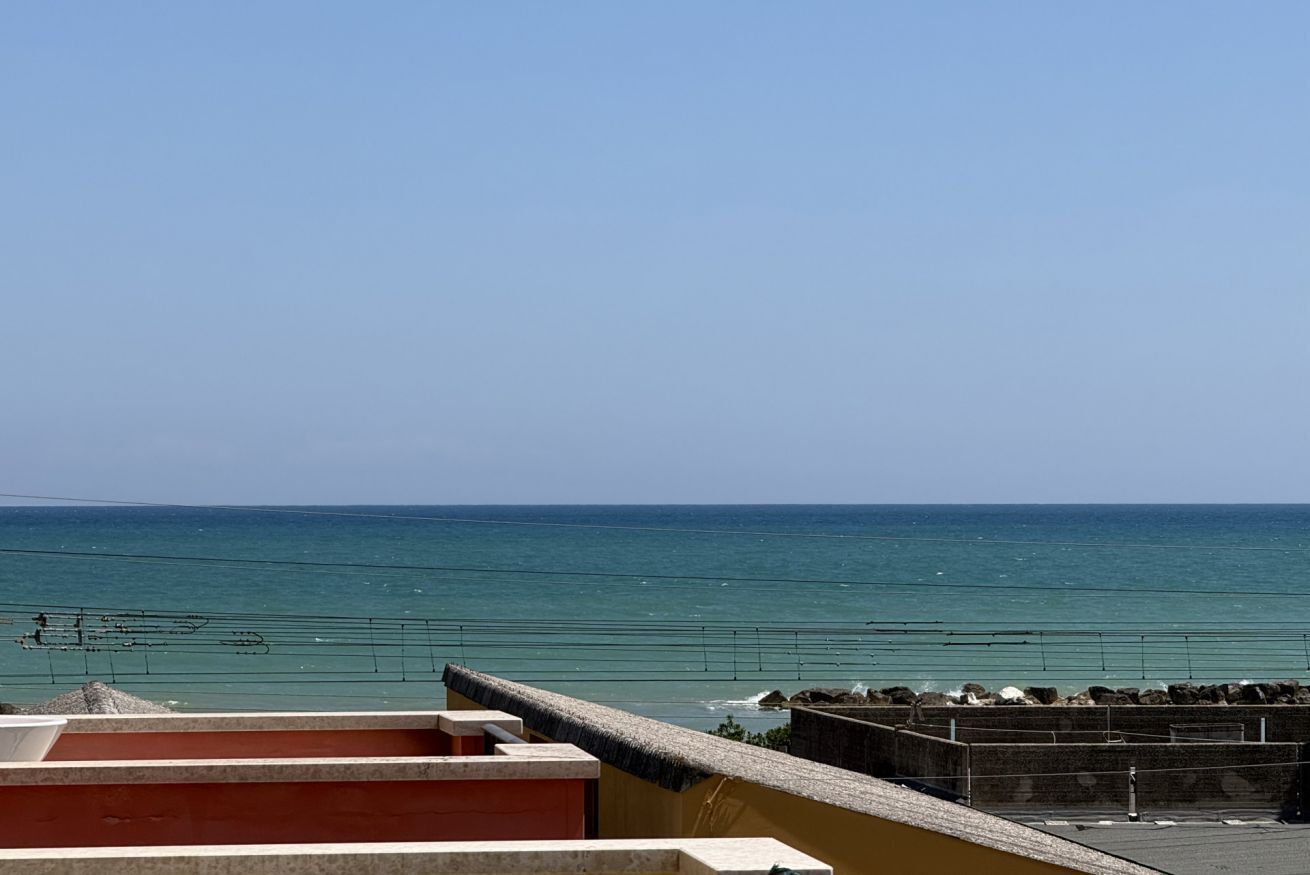 A coastal view with a clear sky, a calm sea, and a stone wall in the foreground.