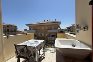 Un balcón con una mesa y una silla, una bañera y vistas a edificios cercanos.
