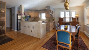 Een ruime keuken met een centraal eiland, houten kastjes en een eethoek met een tafel en stoelen.