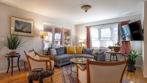 Een woonkamer met een bank, stoelen, een salontafel, een televisie en een boekenkast.
