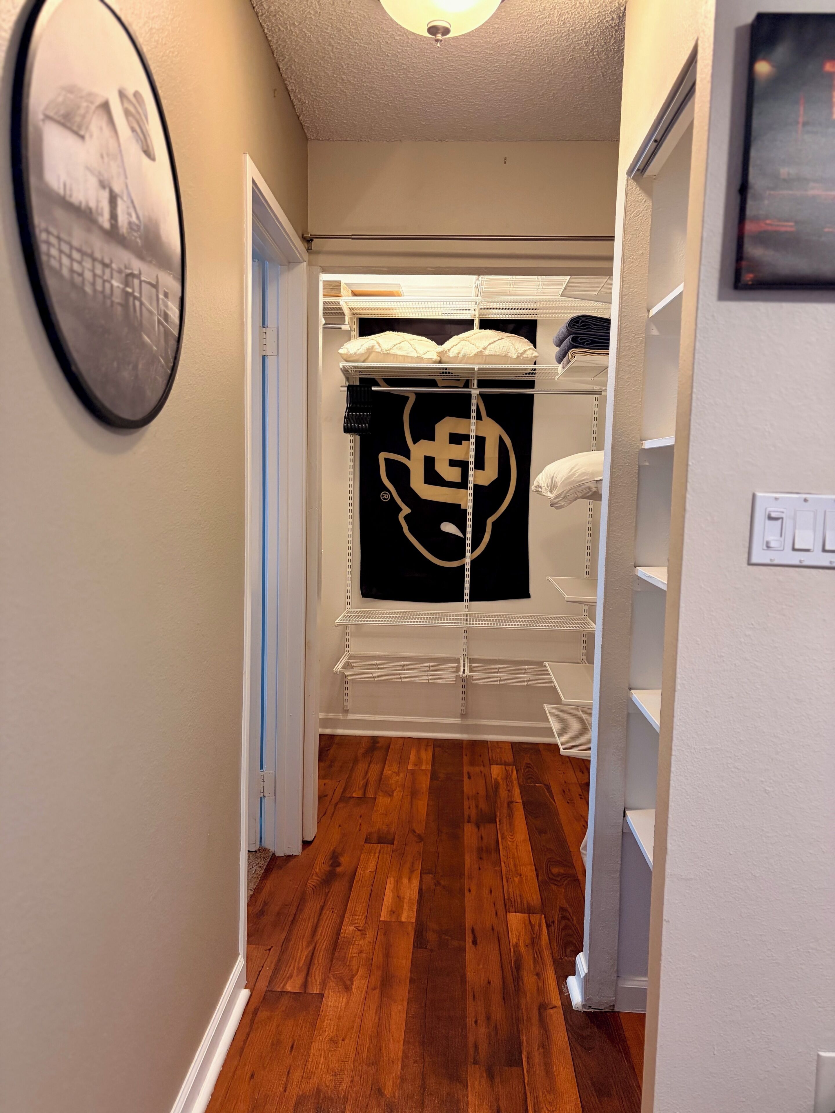 A hallway with wooden flooring, white walls, and a black and white wall decoration.