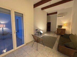 Ein geräumiger Wohnbereich mit Schiebetür, einem Sofa, einem Sessel, einer Lampe und einem Holzkasten.