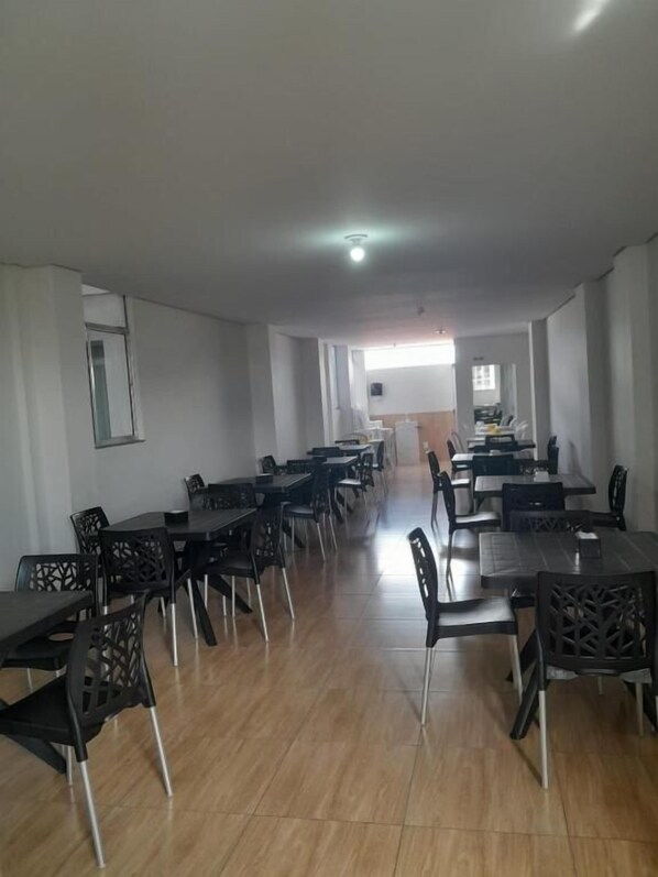 A spacious dining area with multiple tables and chairs, a kitchen in the background, and a ceiling light.
