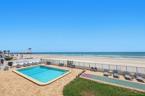 A pool area with a view of the beach, lounge chairs, and a flag. - Oceanfront Daytona Beach Shores Condo - King Suite - Sleeps 6 (Daytona Beach Shores)