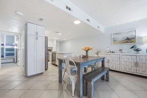 A spacious kitchen with a dining table, white cabinets, and a view of the living area. - Oceanfront Daytona Beach Shores Condo - King Suite - Sleeps 6 (Daytona Beach Shores)
