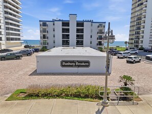 A private parking area with a sign for 'Danbury Breakers' hotel, surrounded by multi-story buildings and a clear sky. - Oceanfront Daytona Beach Shores Condo - King Suite - Sleeps 6 (Daytona Beach Shores)