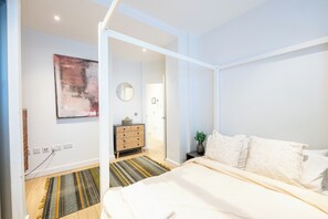 Ein Schlafzimmer mit einem Bett, einem Nachttisch, einem Spiegel, einem Wandbild und einer Tür zu einem anderen Raum.