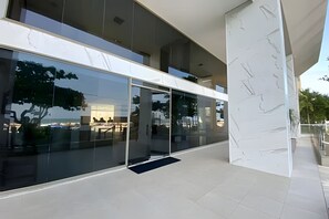 Un edificio moderno con amplios ventanales de vidrio, un pilar de mármol y el reflejo de árboles y un edificio en el cristal.