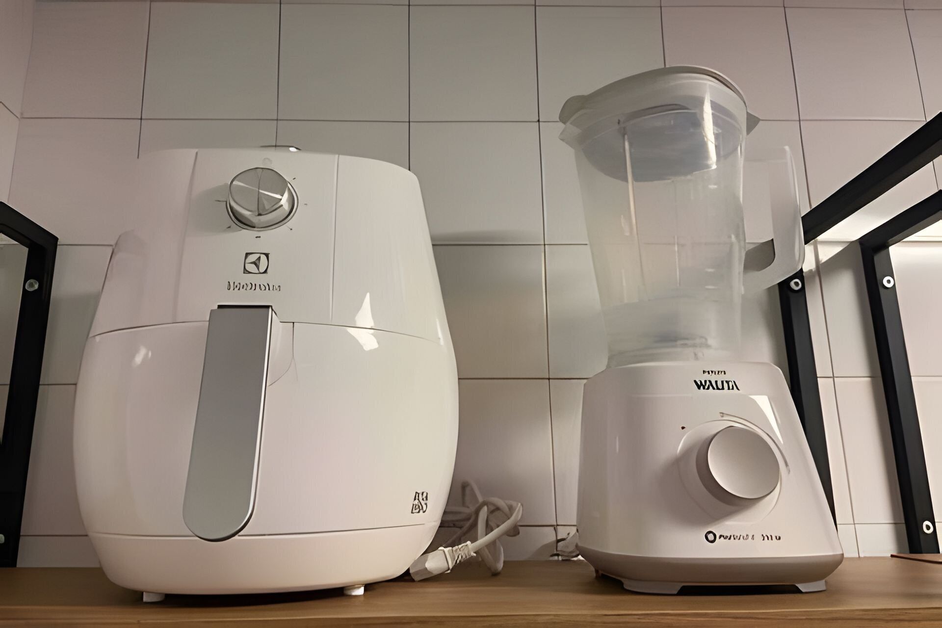 Deux appareils de cuisine blancs, un robot culinaire et un mixeur, sont posés sur un plan de travail en bois, devant un mur carrelé.