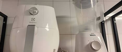 Deux appareils de cuisine blancs, un robot culinaire et un mixeur, sont posés sur un plan de travail en bois, devant un mur carrelé.
