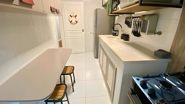 Une cuisine compacte avec un plan de travail blanc, une cuisinière et un réfrigérateur. On y trouve deux tabourets et une petite table.