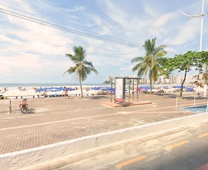 Une promenade en bord de mer bordée de palmiers, avec un arrêt de bus et des parasols de plage.
