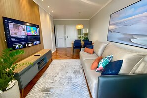 Una sala de estar moderna con televisor de pantalla plana, un sofá, una mesa de centro y un comedor al fondo.