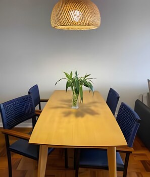 Uma mesa de jantar com seis cadeiras, uma planta em vaso e uma luminária pendente trançada.