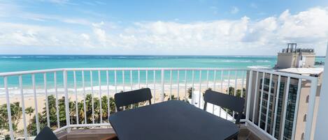 Un balcon avec une table et des chaises donnant sur une plage et l’océan.